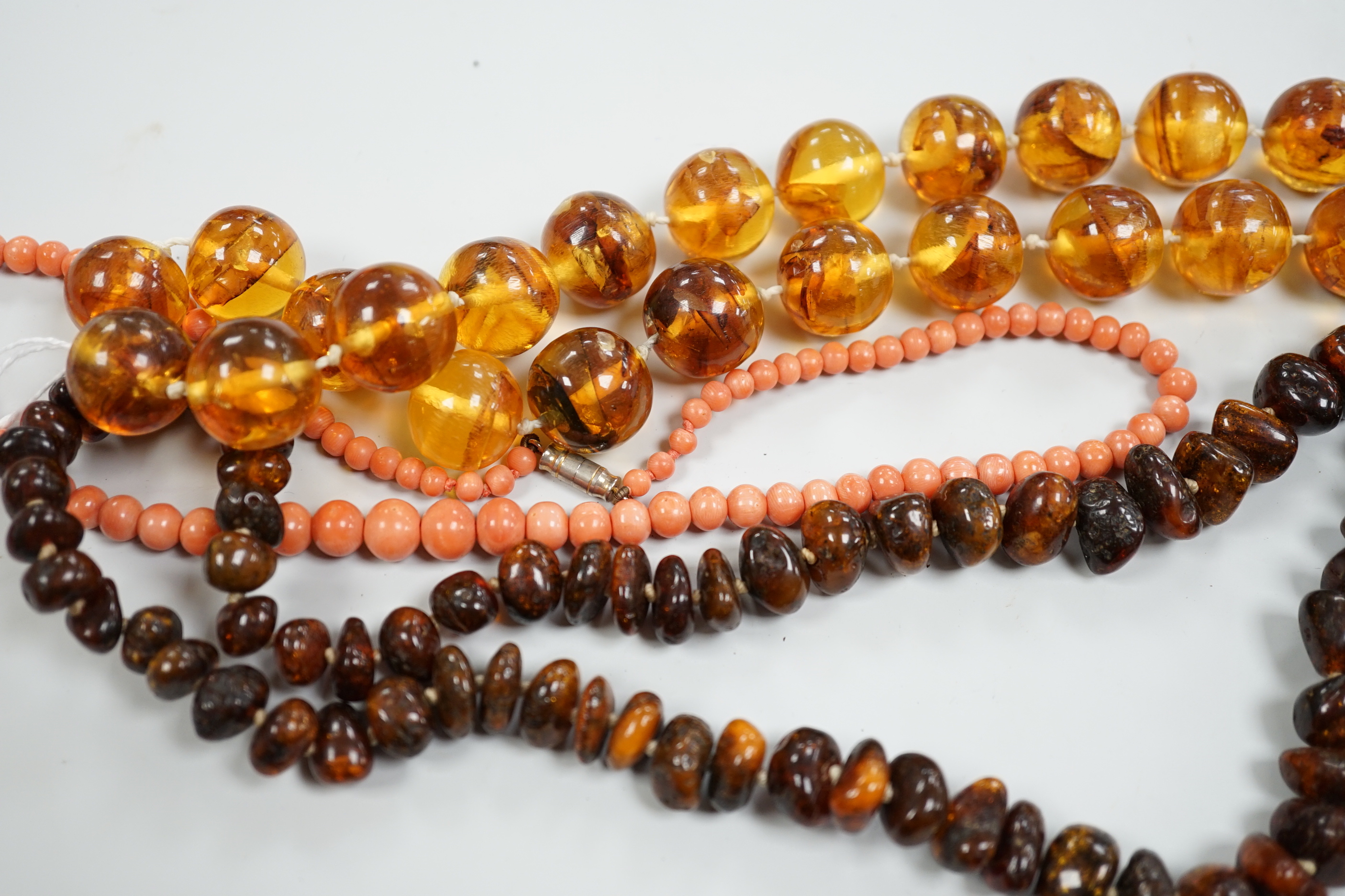 A coral bead necklace, 44cm and two amber bead necklaces.